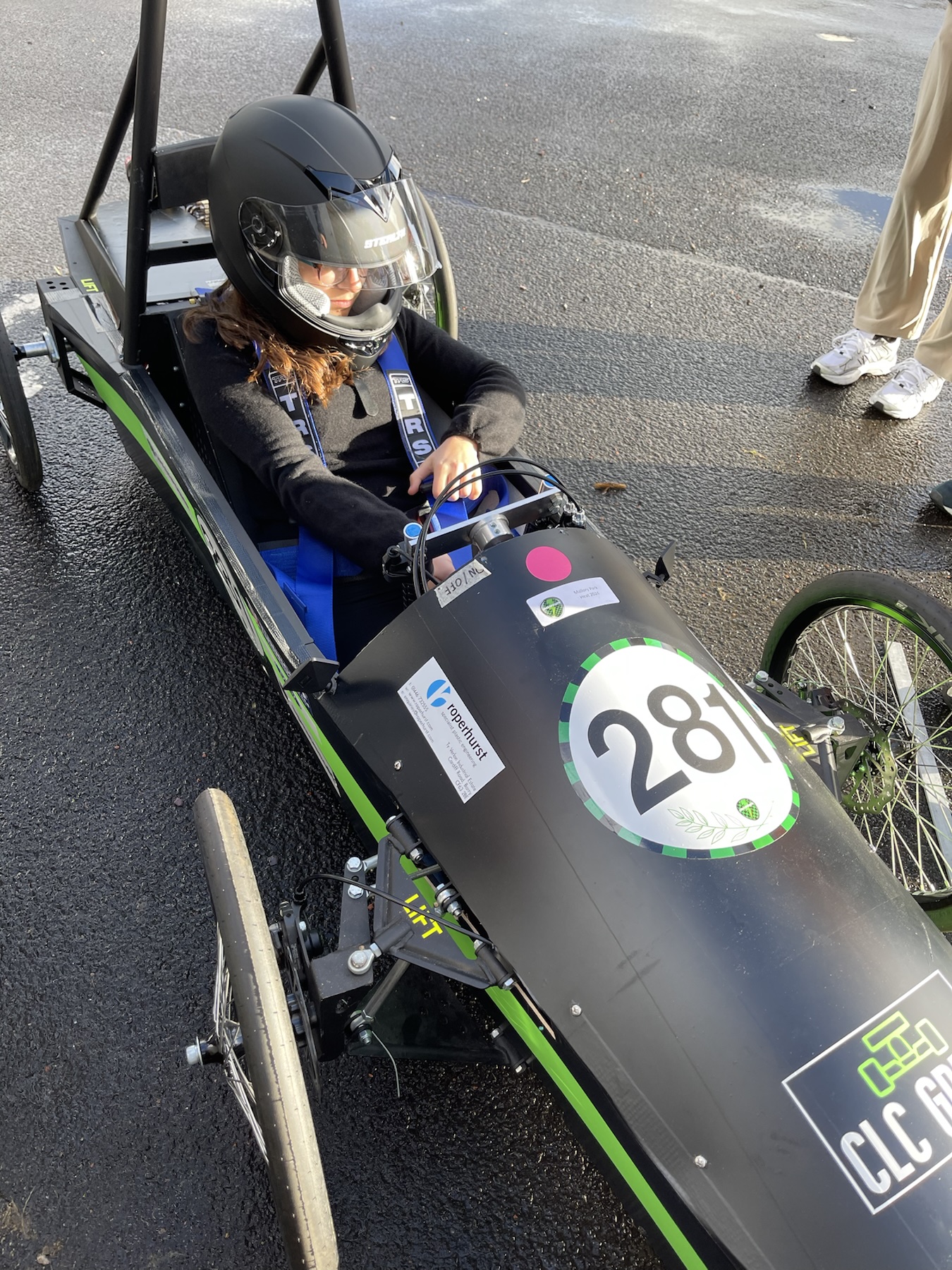 A helmeted driver seated in CLC’s black and green electric race car, number 281, at Aintree